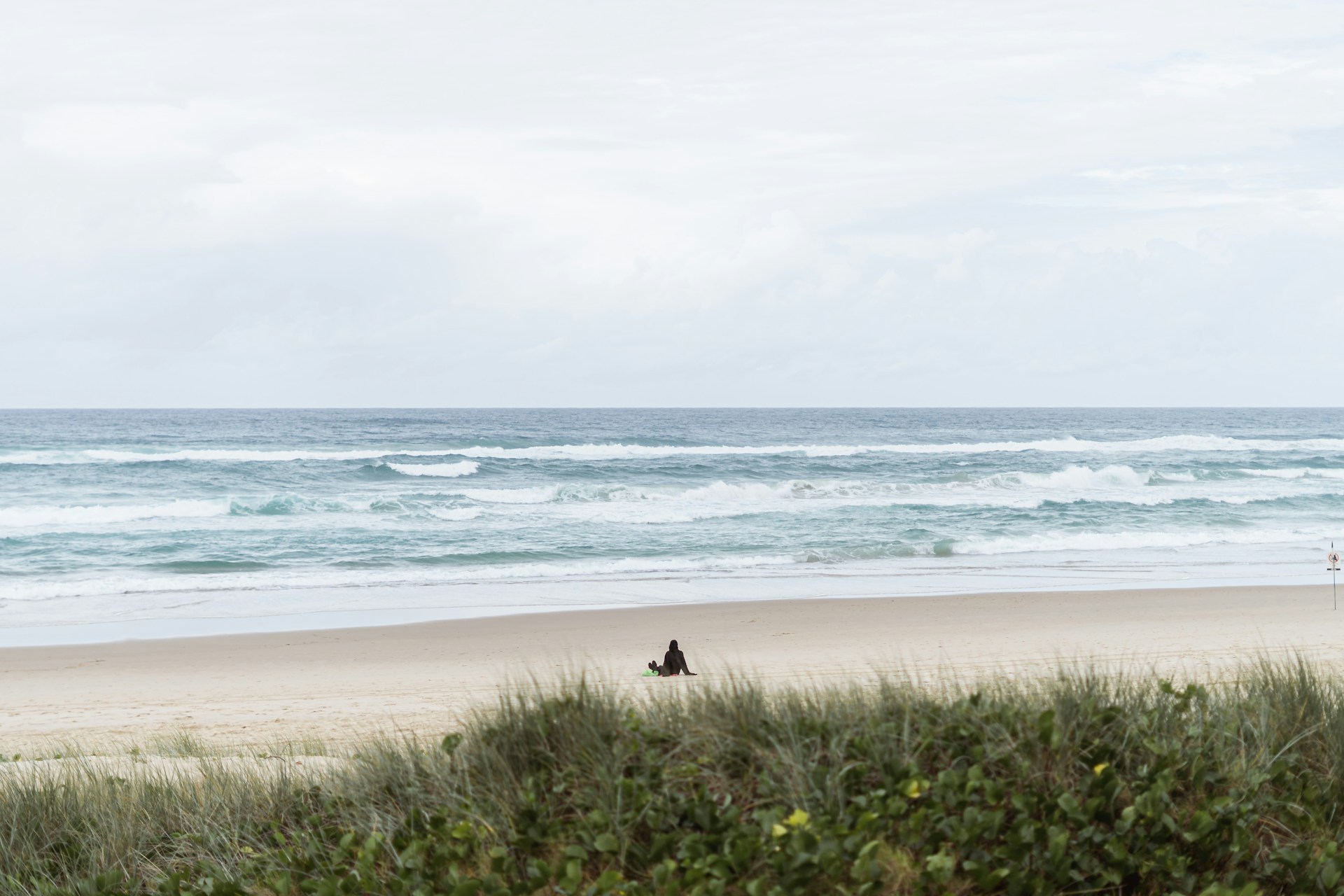 A solitary figure sitting the beach, waves gently rolling in (symbolizing the “slow waves of loss”)